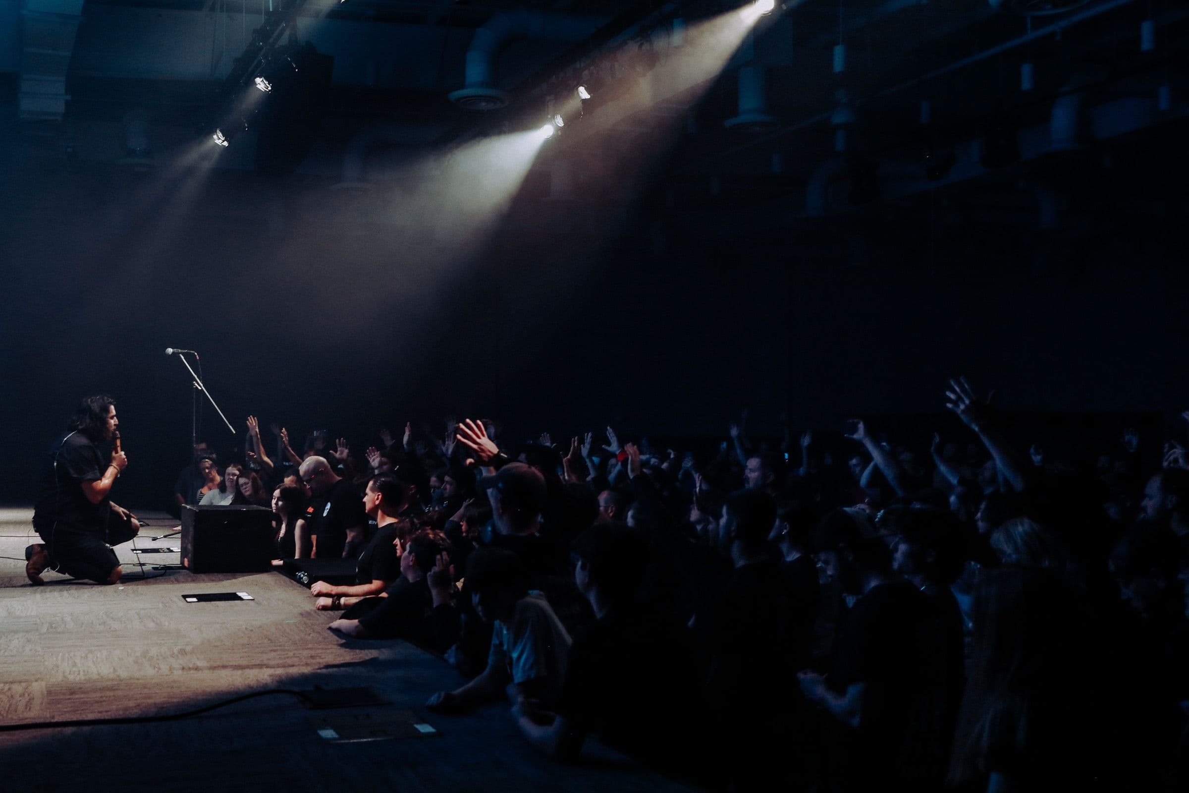 Bloodlines vocalist kneeling at the edge of the stage as the crowd raises their hands